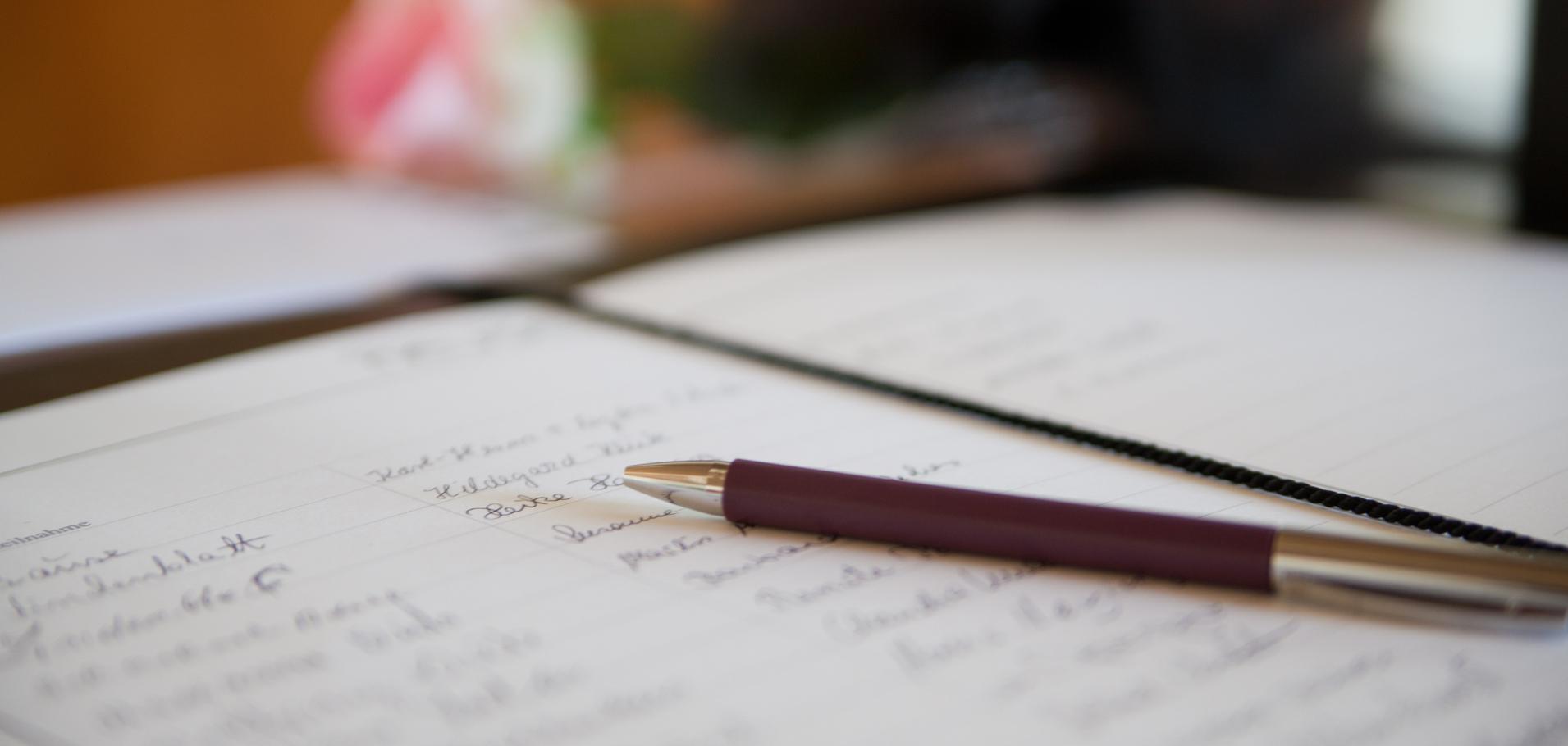 Nahaufnahme eines offenen Notizbuchs mit handschriftlichen Notizen und einem Kugelschreiber auf einem Tisch.