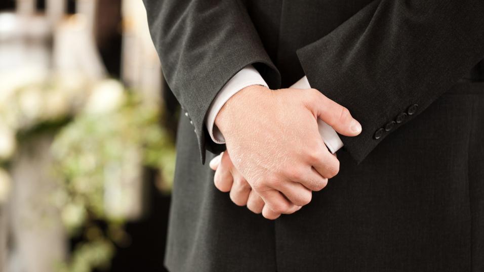 Ein Mann in einem Anzug steht mit verschränkten Händen vor einer dekorierten Kulisse mit Blumen und Kerzen.