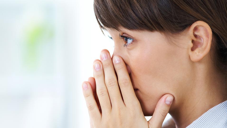 Nahaufnahme einer nachdenklichen Frau, die ihre Hände vor dem Gesicht hält und in die Ferne blickt.