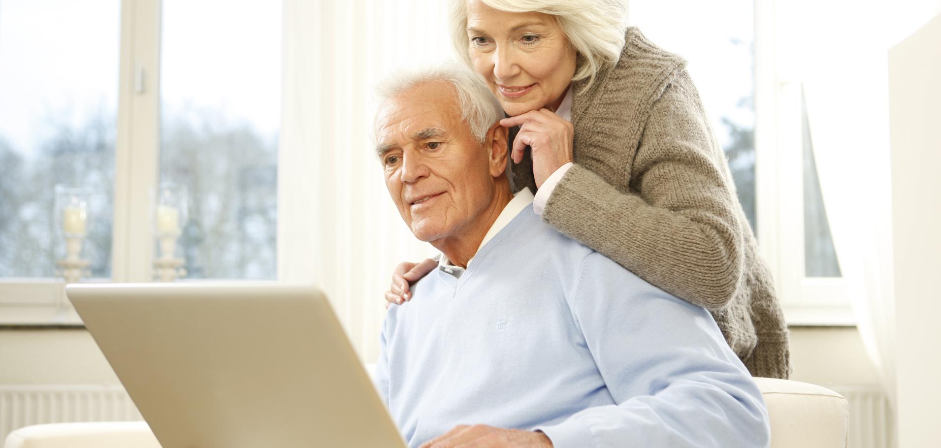 Paar sitzt auf einer Couch und schaut gemeinsam auf einen Laptop in einem hellen Raum.